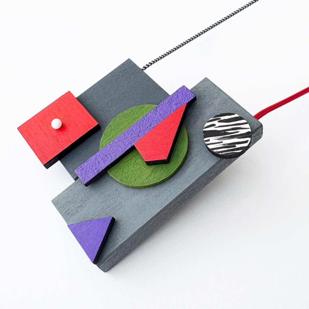 Red, purple and green geometric wooden necklace with layered shapes on a white background