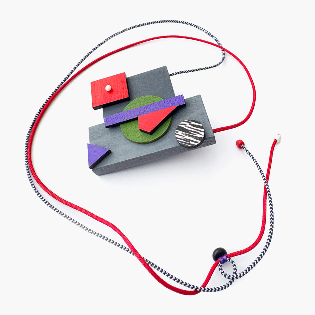 Full view of red, purple and green geometric wooden necklace with adjustable cords