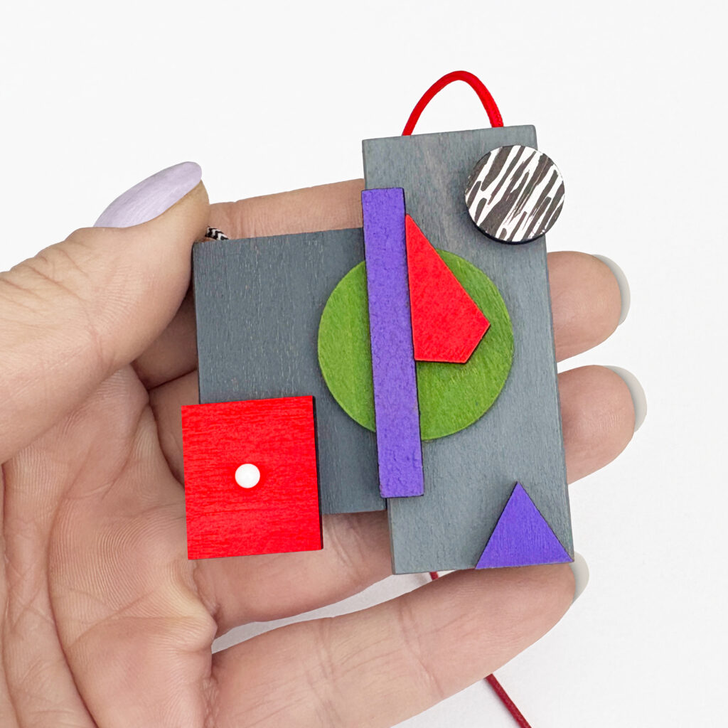 Red, purple and green geometric wooden necklace shown in hand for scale