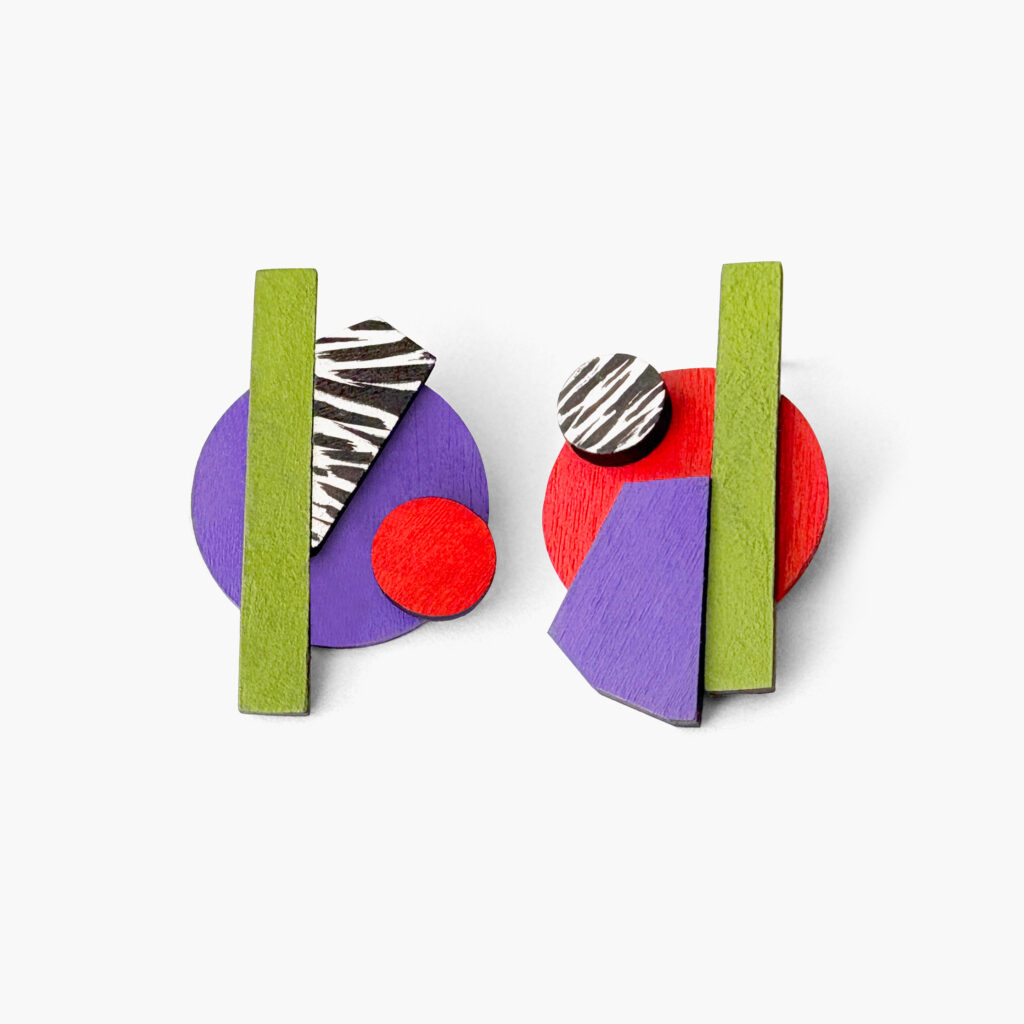 Abstract purple and green mismatched statement earrings with purple, green, red and black-and-white layered shapes on a white background