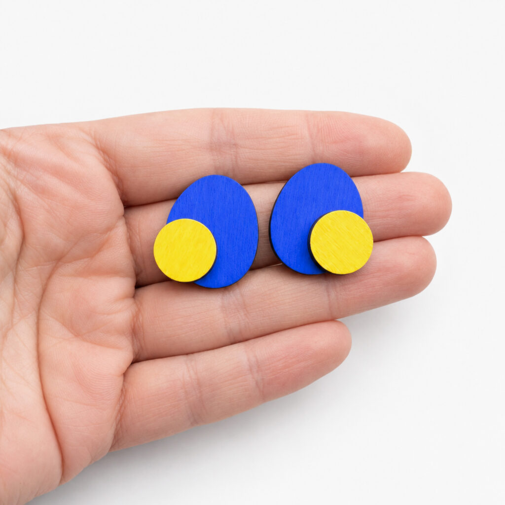 Blue and yellow geometric stud earrings – handmade wooden jewelry in hand for scale