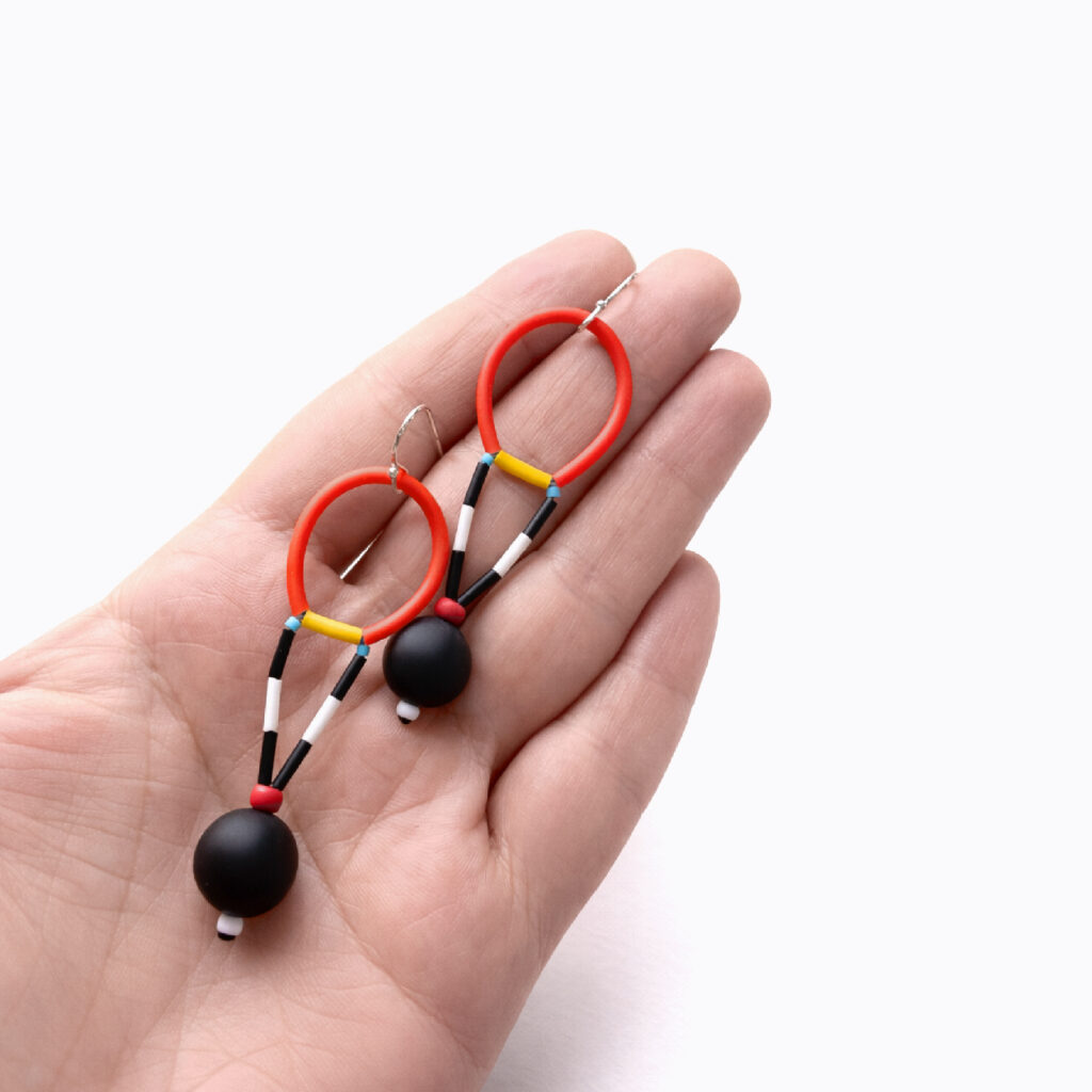 Pair of red and black beaded dangle earrings with geometric wooden elements shown in hand