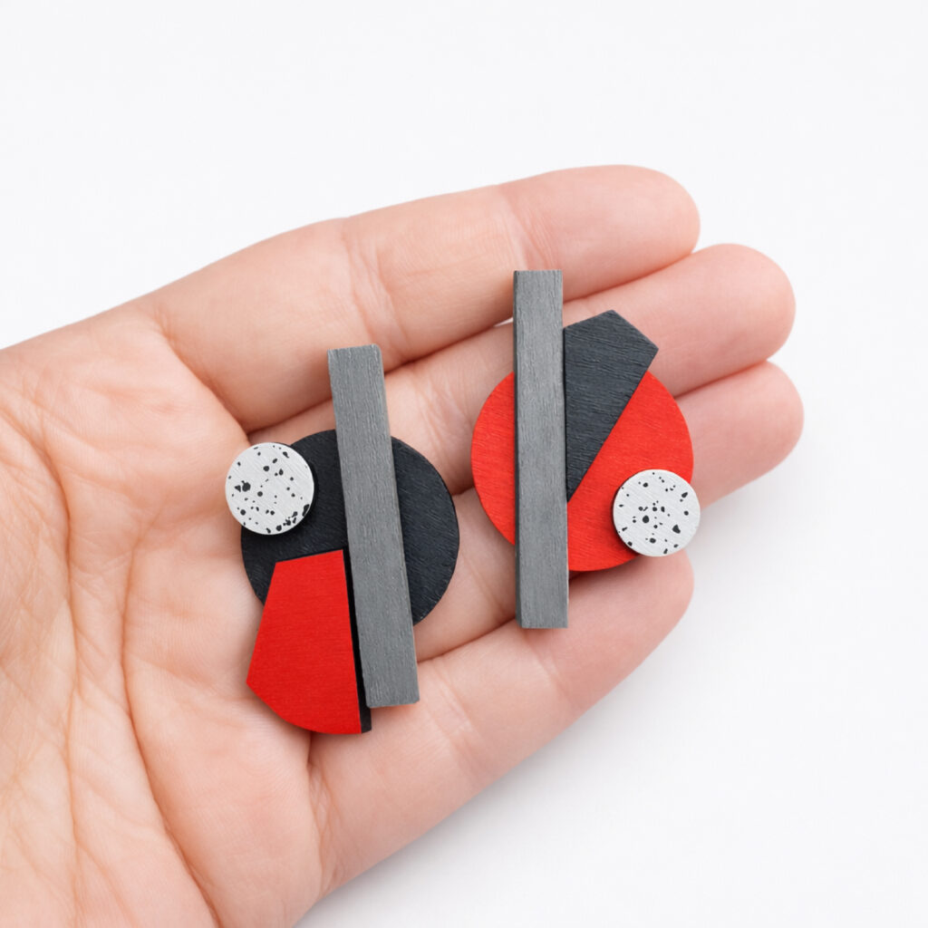 Red black and grey mismatched geometric wooden earrings shown in hand