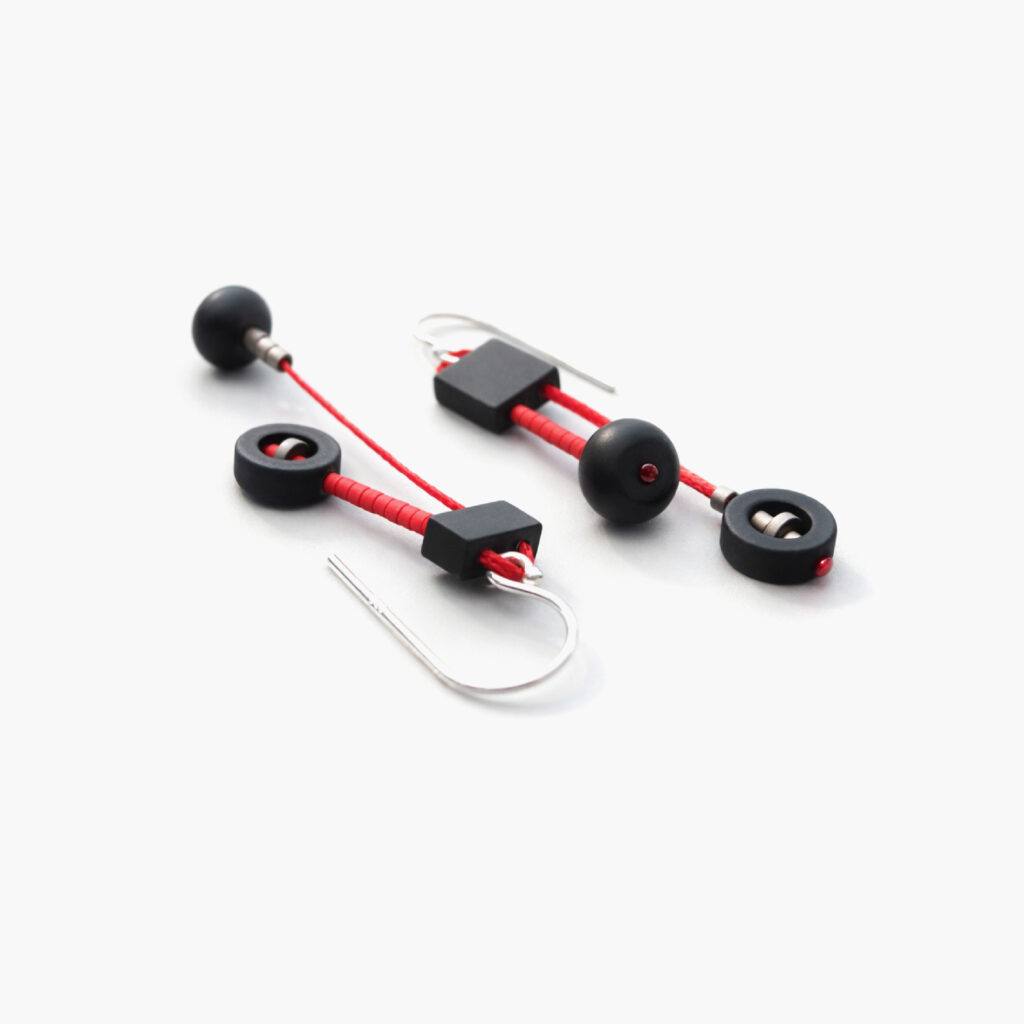 Pair of black and red geometric dangle earrings arranged diagonally on white background