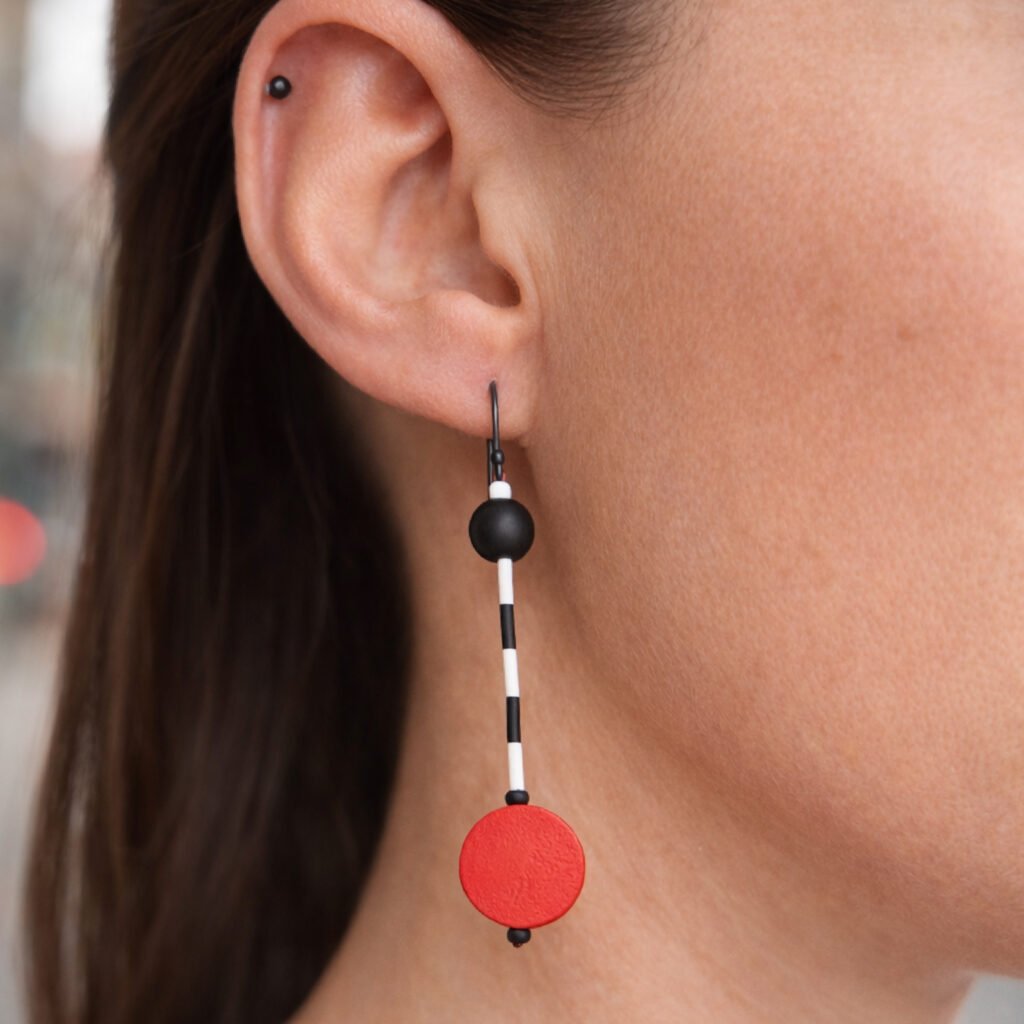 Red and black mismatched geometric dangle earring worn on ear