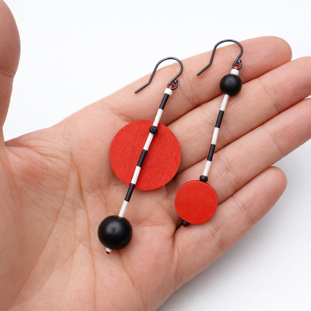 Asymmetrical red and black wooden earrings with matte black beads shown in hand