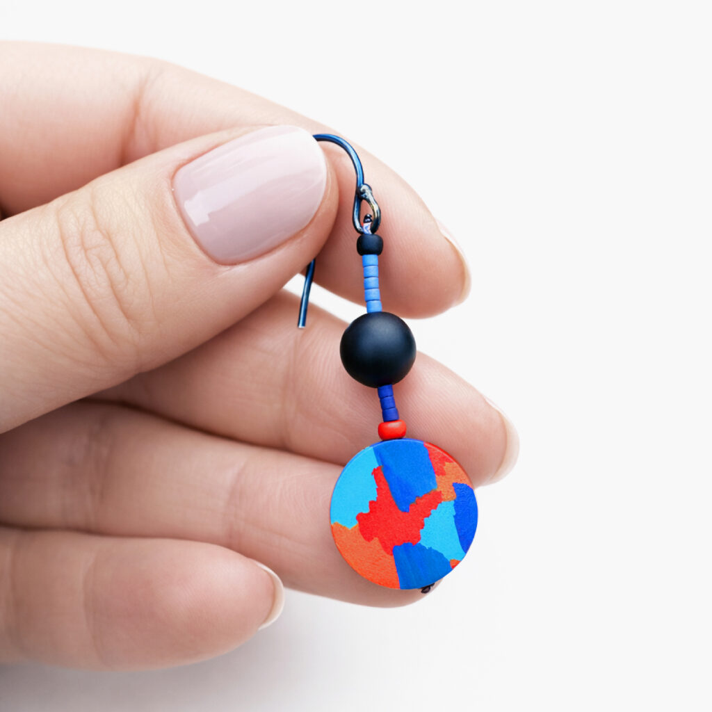 Red and blue geometric wooden dangle earring held between fingers
