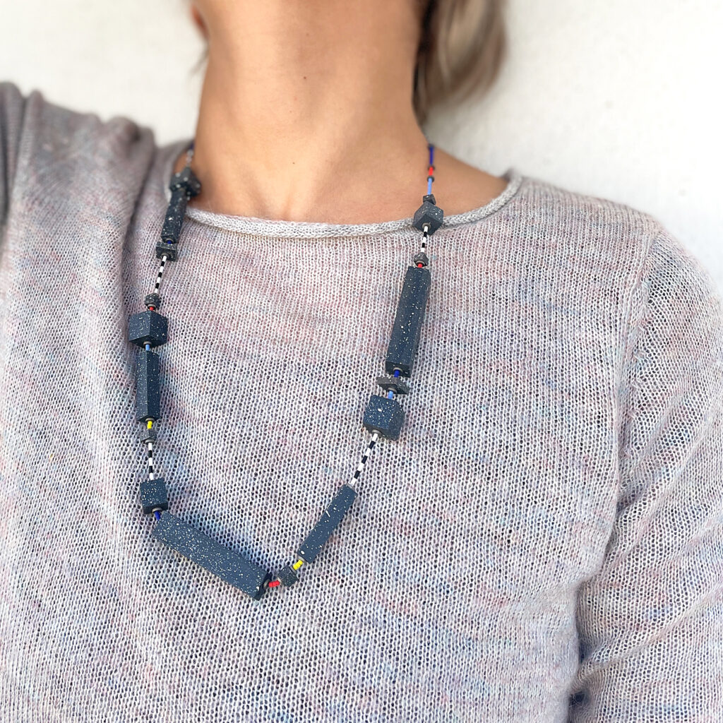 Geometric statement necklace with multicolored accents worn with a grey top