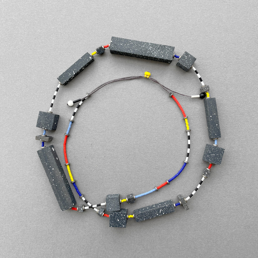 Speckled geometric statement necklace arranged in a circular composition showing its wooden elements on grey background