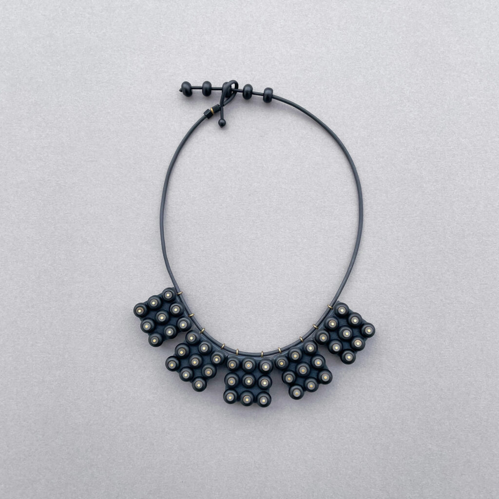 Black onyx and geometric wooden statement necklace displayed on grey background