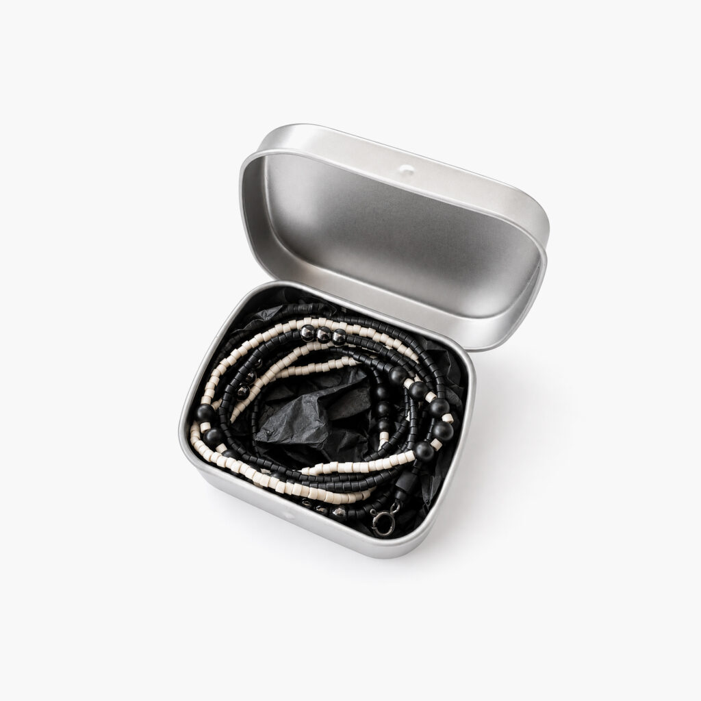 Black and white minimalist beaded necklace coiled in a metal gift box