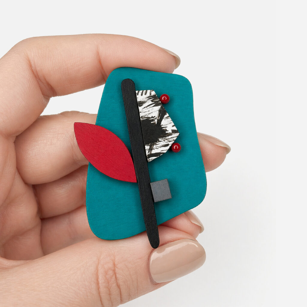 Hand-painted geometric wooden brooch held in hand