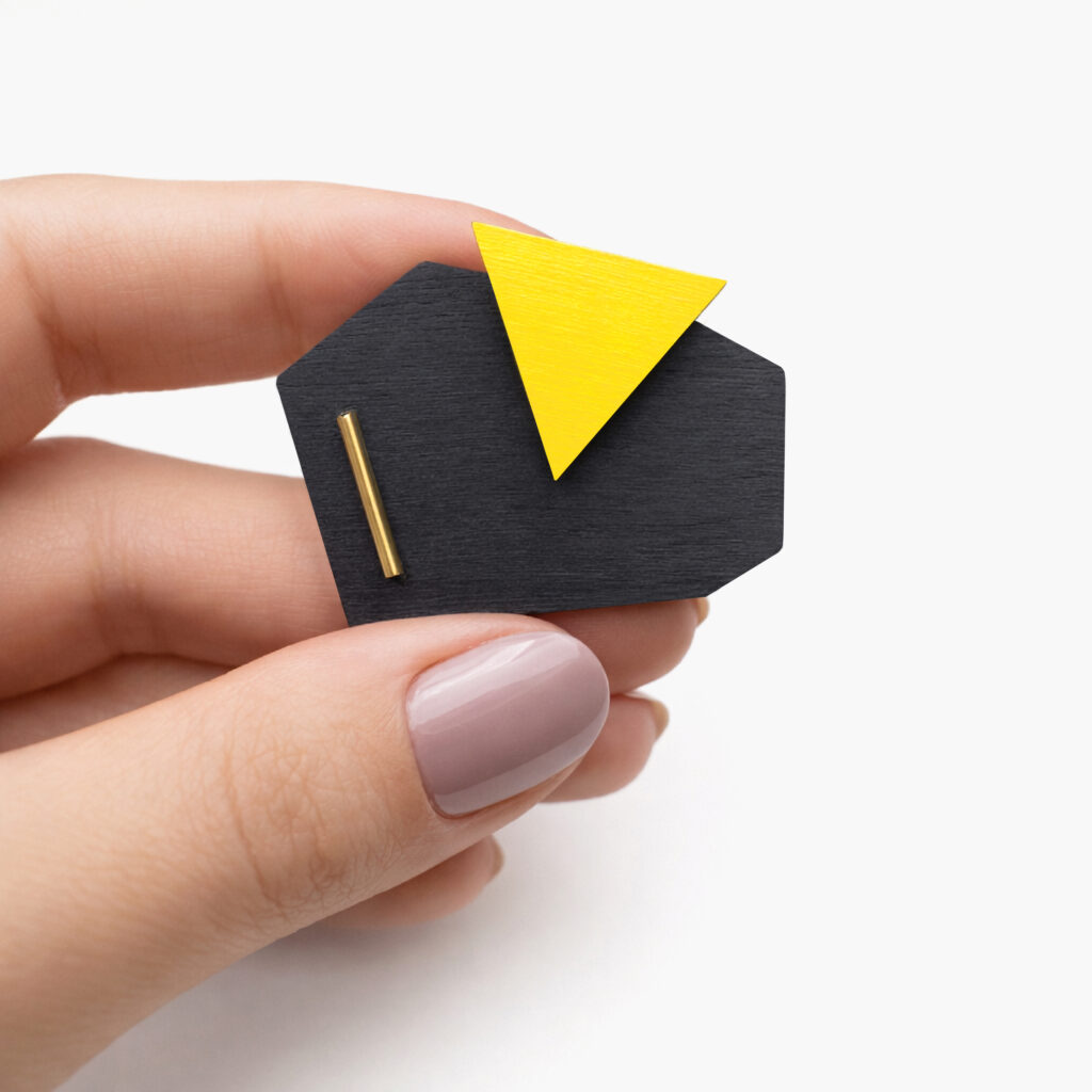 Black and yellow geometric wooden brooch shown in hand for scale