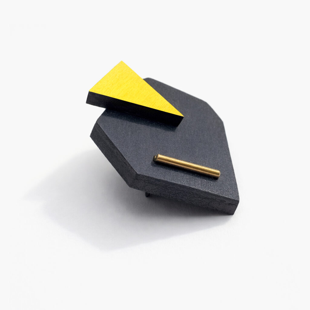 Side view of black and yellow geometric wooden brooch showing its layered construction