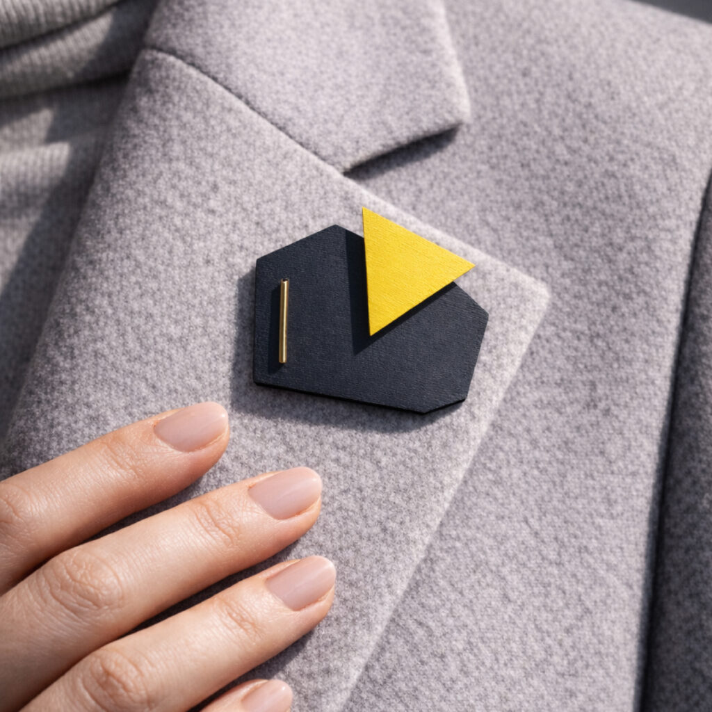 Black and yellow geometric wooden brooch worn on a grey blazer